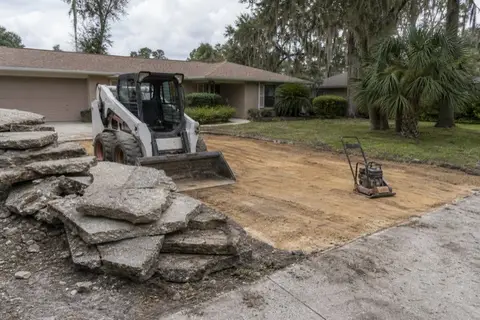 Broken slabs stacked beside exposed sandy subgrade during a driveway tear-out