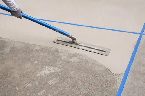 Trowel spreading a pale polymer overlay across an older concrete slab